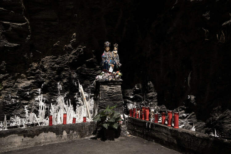 A colorful statue of the Madonna and Child on a stone pedestal in a cave.