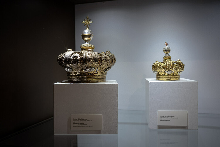 Two ornate golden crowns seen inside a museum case.